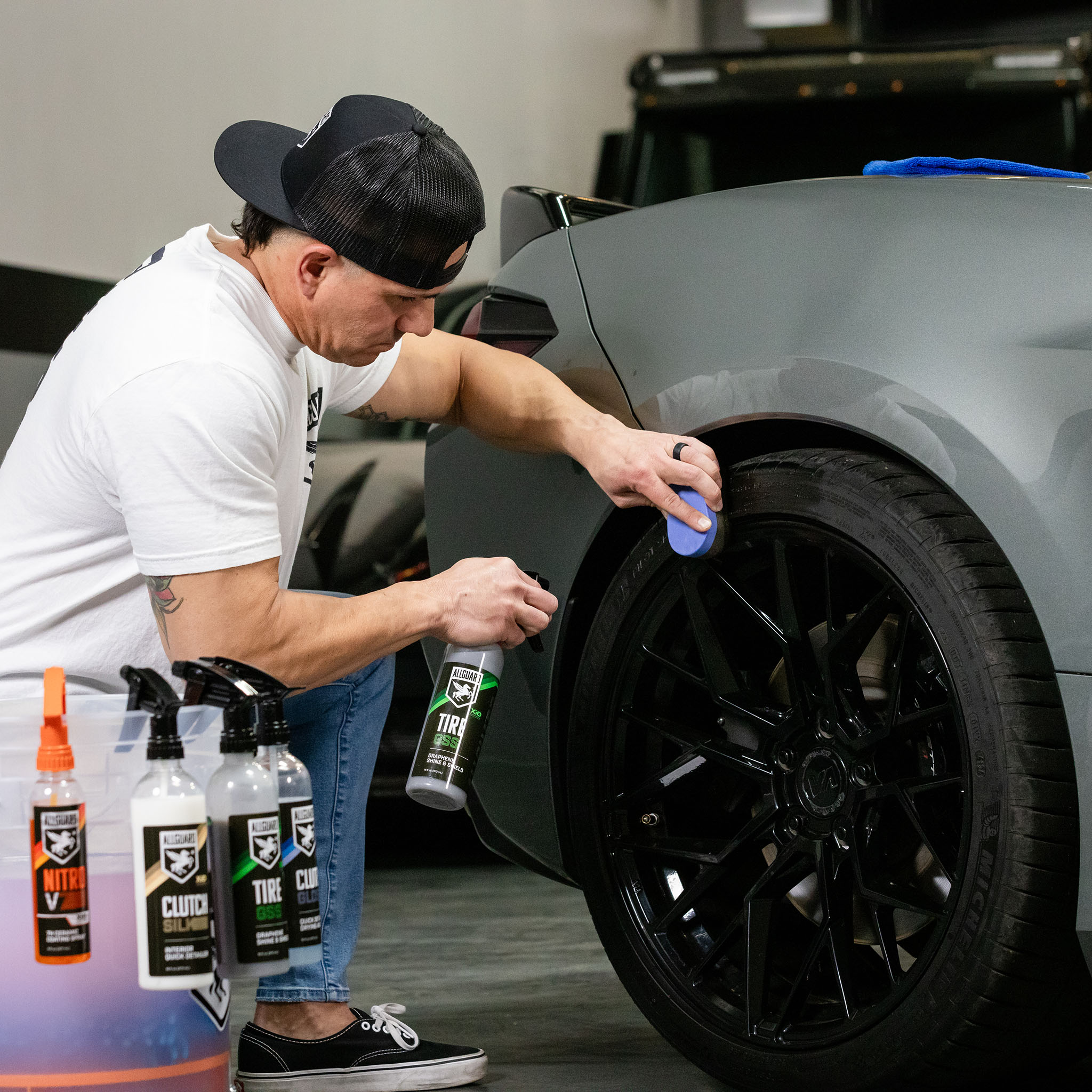 Man in backwards hat polishes tires to a noticeable shine during exterior car detail