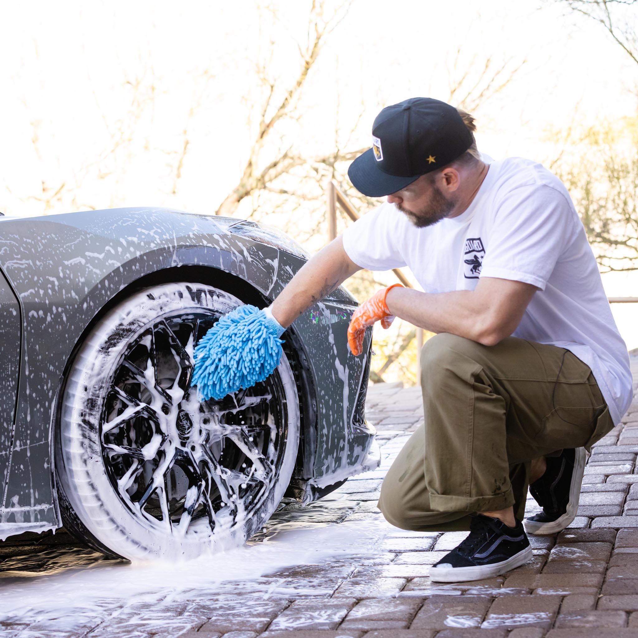 Man wearing car wash mitt shampoo cleaning satin black patterned rims