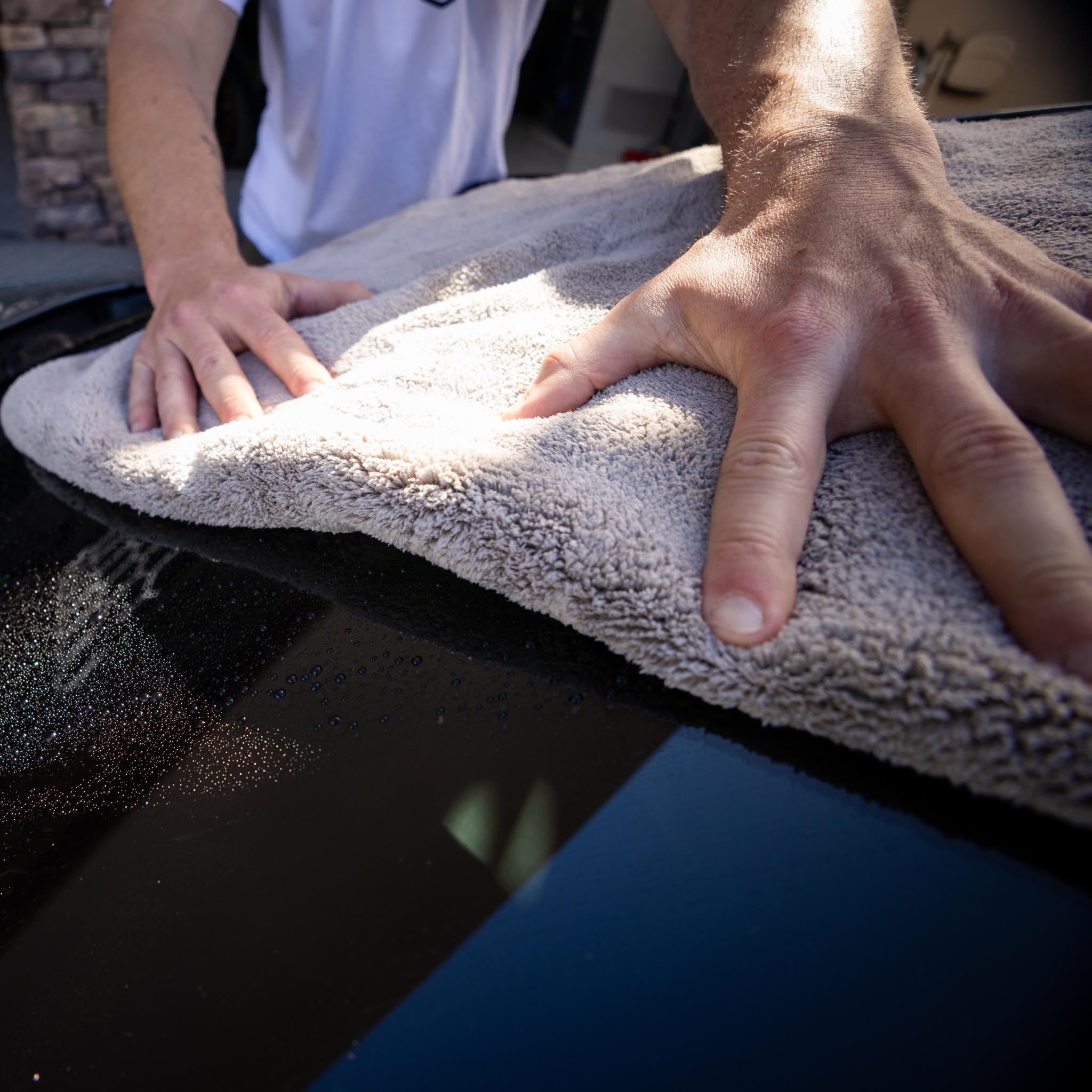 Man uses thick absorbent detailing towel on rear of car