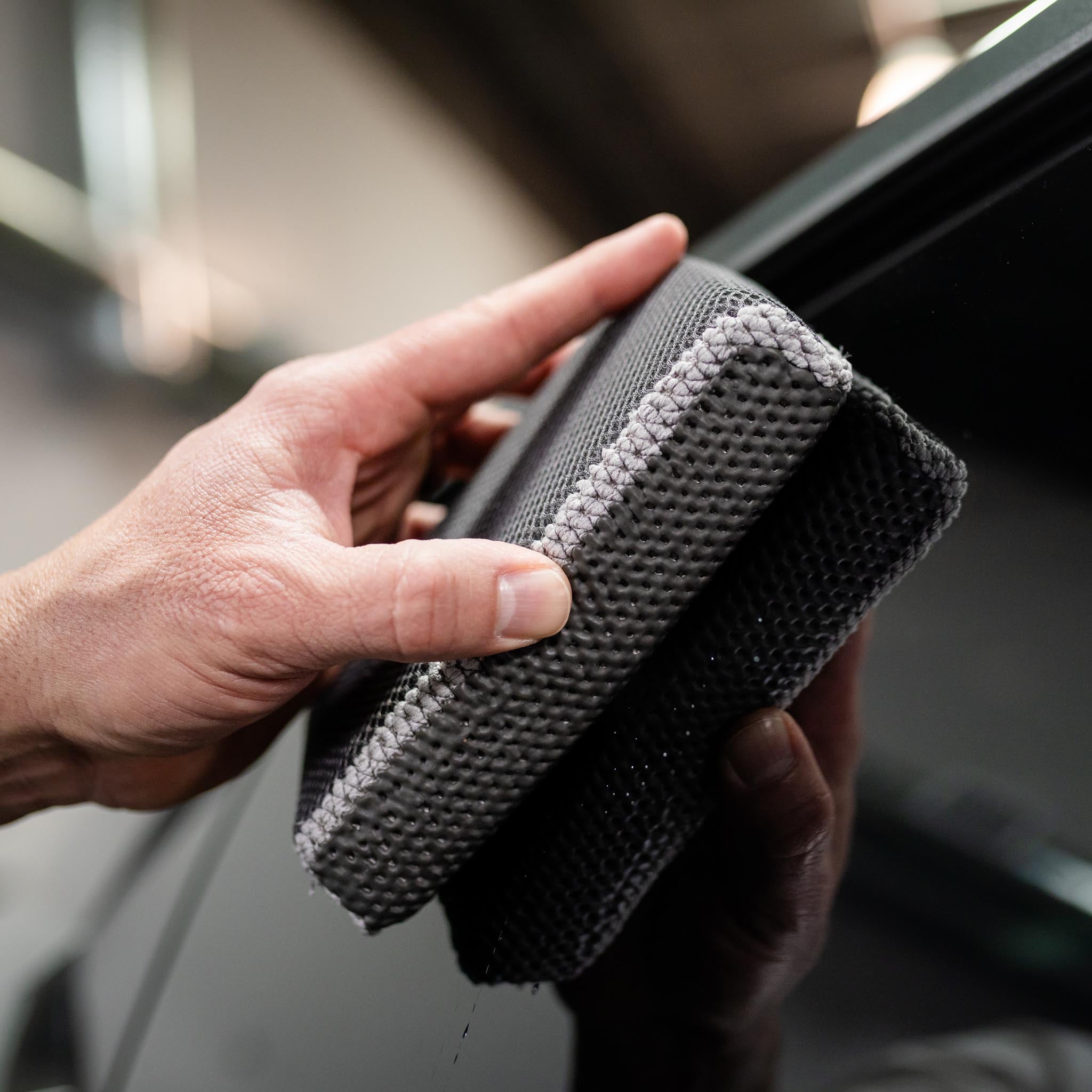 Hand holding clay scrubber decon washing black car