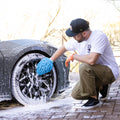 Man wearing car wash mitt shampoo cleaning satin black patterned rims 
