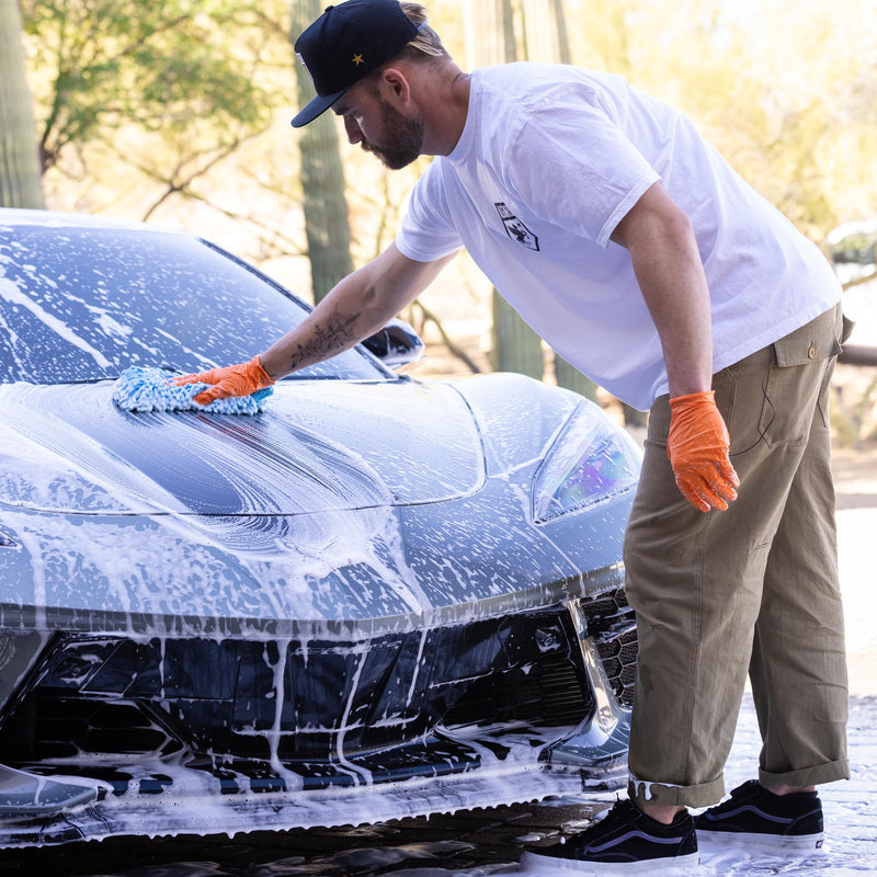 Bearded man focuses on washing hood of sports car